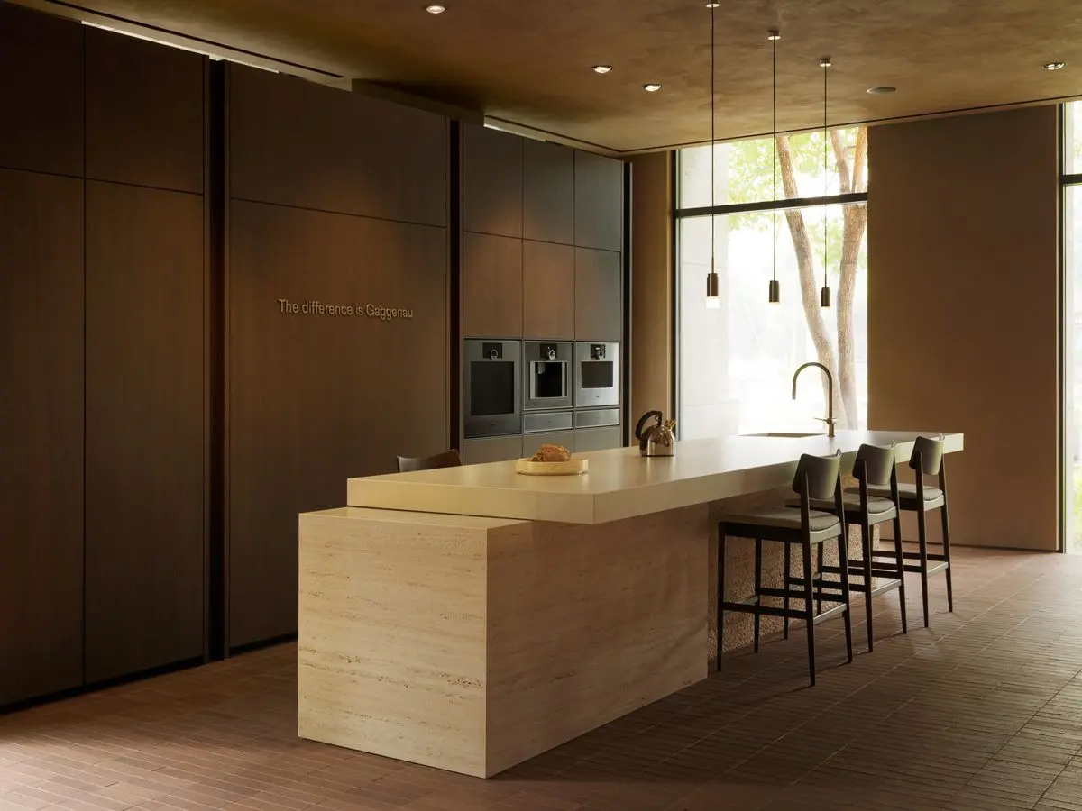 Minimalistična kuhinja v showroomu Gaggenau Taipei z velikim svetlim otokom in temnimi vgradnimi omarami.